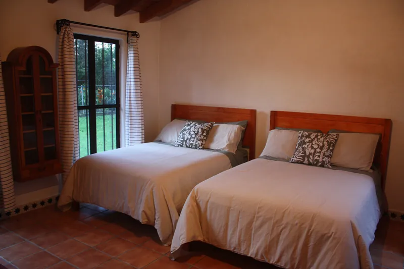 Recámara con dos camas matrimoniales y ventana al jardín